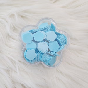 May include: A clear plastic flower-shaped container filled with light blue cloud-shaped confetti.