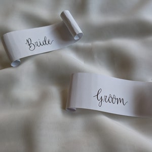 May include: Two white paper scrolls with black calligraphy. The top scroll says "Bride" and the bottom scroll says "Groom".