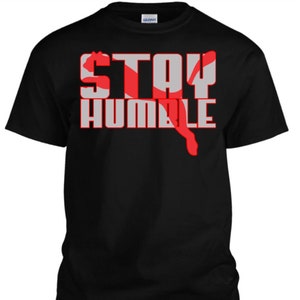 May include: Black t-shirt with the words "STAY HUMBLE" in red and white letters. The letters are layered over a red and white graphic of a puma.
