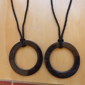 Puede incluir: Dos colgantes circulares negros con cordones negros que cuelgan de ellos. Los colgantes están hechos de un material liso y brillante.