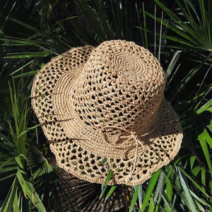 Puede incluir: Un sombrero de sol de crochet de color marrón claro con un ala ancha y un lazo atado.