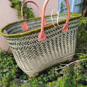 May include: A woven basket featuring a green and light tan herringbone pattern with a dark green rim. The basket includes two tan leather handles attached with metal rivets and white stitching, along with small leather corner reinforcements.