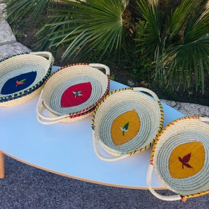 Peut inclure: Quatre paniers tissés avec des poignées, chacun présentant un motif de feuille de couleur différente. Les feuilles sont brodées avec du fil coloré et comprennent une feuille bleue, rouge, jaune et orange.