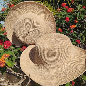Peut inclure: Deux chapeaux en paille de couleur beige clair avec des bords larges et circulaires et des calottes arrondies. Les chapeaux présentent un motif concentrique étroitement tissé sur toute la matière, créant une texture uniforme.