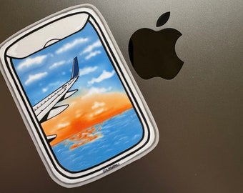 May include: A sticker of a phone screen showing a view from an airplane window. The window shows a blue sky with white clouds, a sunset over the ocean, and the wing of an airplane. The sticker has a white border and the text "@artmotive_" in the bottom right corner.
