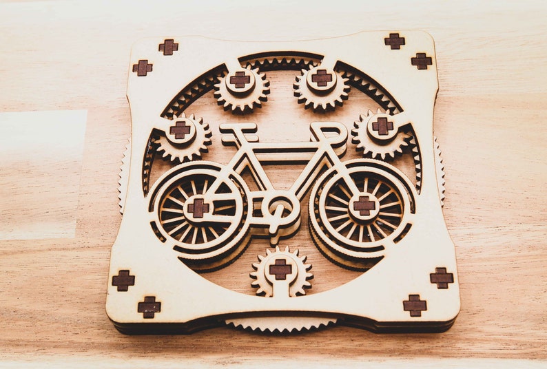 May include: A wooden model of a bicycle with gears, the wheels are made of wood and have a brown cross pattern in the center. The bicycle is surrounded by smaller gears.