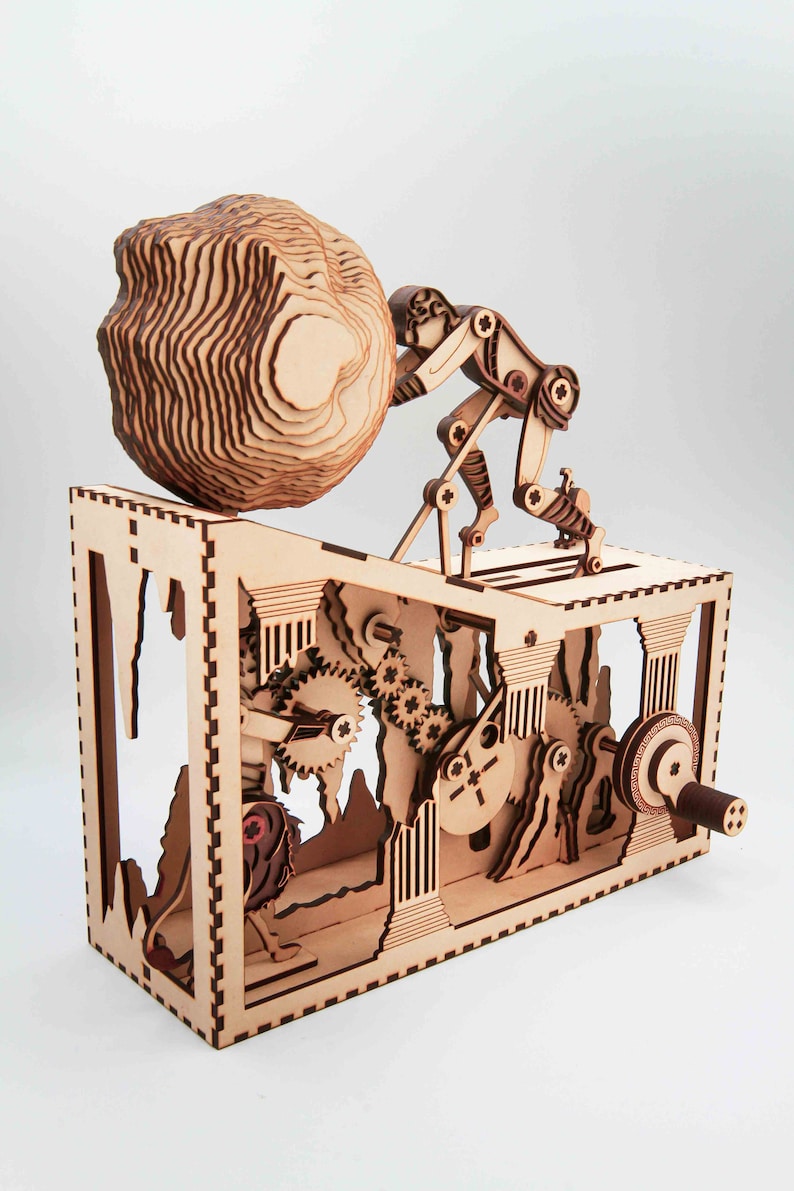 May include: A wooden kinetic sculpture of a robot pushing a large, round rock up a hill. The sculpture is made of laser-cut wood and features intricate details, including gears, wheels, and a winding path. The robot is made of multiple pieces of wood that are connected by joints, allowing it to move.