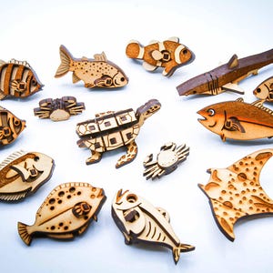 May include: A collection of wooden marine life figures, including fish, a shark, a turtle, and a stingray. The figures are intricately cut and feature natural wood tones with darker detailing, creating a charming, handcrafted aesthetic.