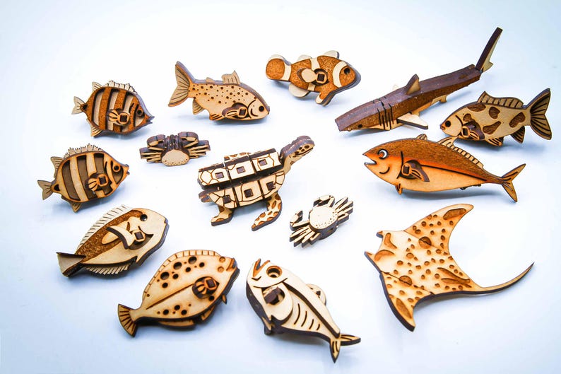 May include: A collection of wooden marine life figures, including fish, a shark, a turtle, and a stingray. The figures are intricately cut and feature natural wood tones with darker detailing, creating a charming, handcrafted aesthetic.