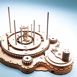May include: A wooden model of a mechanical device with gears, wheels, and vertical rods. The model has a complex design with multiple layers and circular components. The color is natural wood, and the background is a gradient of blue and white.