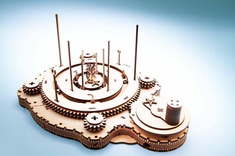 May include: A wooden model of a mechanical device with gears, wheels, and vertical rods. The model has a complex design with multiple layers and circular components. The color is natural wood, and the background is a gradient of blue and white.