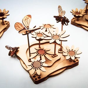 May include: Wooden laser-cut decorative pieces featuring flowers and butterflies. The pieces are light brown with intricate details, including layered bases and delicate insect and flower designs. The overall theme is nature and garden.