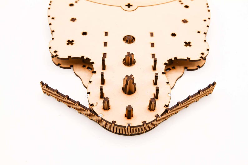 May include: A laser-cut wooden puzzle, featuring a complex design with multiple interlocking pieces. The puzzle has a light brown color and is made of thin wooden sheets. The design includes various shapes and patterns, with a focus on precision and detail.