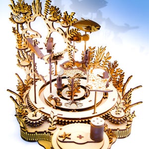 May include: A wooden, laser-cut model of an underwater scene, featuring fish, coral, and other marine life. The model has a circular base with gears and a detailed, layered design. The natural wood color is prominent.