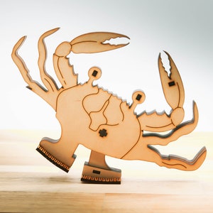 Può includere: Una statuetta di granchio in legno con gambe articolate e un design dettagliato. Il granchio è in piedi su una base di legno.