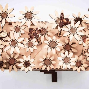 Può includere: Opera d'arte da parete in legno con un design floreale di margherite e farfalle. L'opera è realizzata in legno chiaro con dettagli intricati, tra cui api e farfalle. Il pezzo ha una forma rettangolare e misura circa 46 cm di larghezza e 30 cm di altezza.