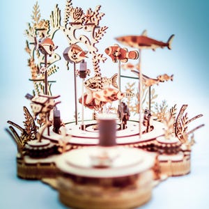 May include: A wooden, laser-cut model of an underwater scene, featuring various fish, coral, and seaweed. The model is constructed from light-colored wood and includes a shark, clownfish, and other marine life. The design is intricate and detailed.