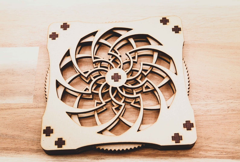 May include: A wooden geometric design with a spiral pattern. The design is made of multiple layers of wood, creating a three-dimensional effect. The wood is a light brown color, and the design is accented with small, dark brown squares.