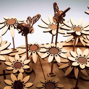 May include: Wooden laser-cut daisies and bees. The flowers have light-colored petals and a dark brown center. The bees are also made of wood and have detailed wings. The scene is set against a light background.