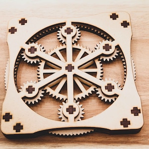 May include: A wooden gear puzzle with a square frame and multiple interlocking gears. The gears are made of light brown wood and have dark brown accents.