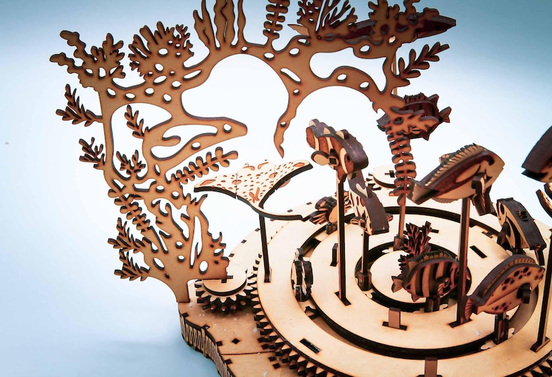 May include: A wooden, laser-cut model of an underwater scene, featuring coral, fish, and other marine life. The model is made of light brown wood and has intricate details, including cut-out designs and layered elements.