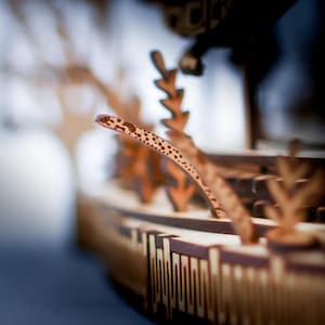 May include: A detailed wooden model of a ship, featuring intricate cut-out designs and a curved, patterned element. The model is primarily brown with lighter accents, showcasing a focus on craftsmanship and detail.