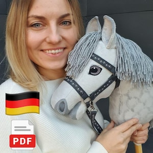 May include: A light gray hobby horse toy featuring a soft fabric head, a thick gray yarn mane, and a black bridle with white decorative stitching. The horse has dark embroidered eyes and is attached to a wooden stick handle for play.