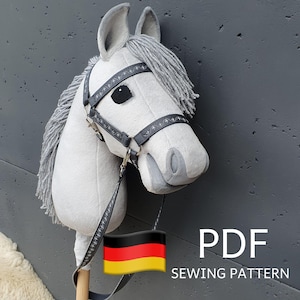 Op de afbeelding: Een grijs en wit pluche paardenhoofd met een zwart hoofdstel en een Duitse vlag. Het paardenhoofd is bevestigd aan een houten stok. De tekst "PDF SEWING PATTERN" is onder de afbeelding gedrukt.