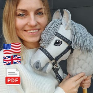 May include: A light gray hobby horse toy featuring a soft plush head with a dark gray bridle, a long gray yarn mane, and embroidered eye details. The horse is mounted on a wooden stick and includes a matching gray lead rope with decorative trim.