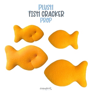 May include: Four orange plush fish-shaped props with a textured surface. The text PLUSH FISH CRACKER PROP is displayed at the top, and the text dreamyferret is at the bottom. The fish are arranged in two pairs, each with a distinct shape and size.