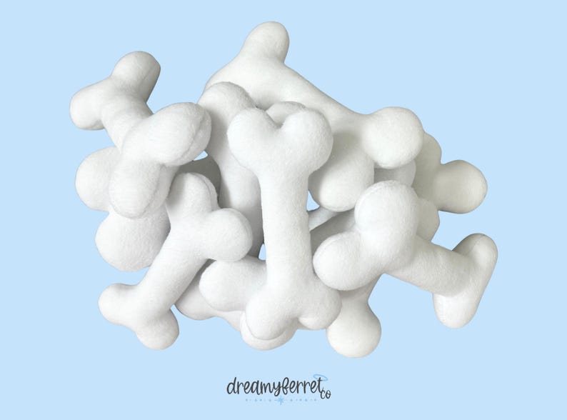 May include: A pile of white, plush bone-shaped toys against a light blue background. The toys are soft and rounded, with a three-lobed shape at each end. The logo "dreamyferret.co" is visible in the bottom right corner.