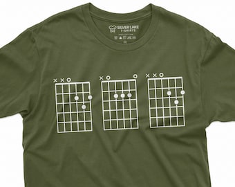 Könnte beinhalten: Ein grünes T-Shirt mit drei Gitarrenakkorddiagrammen, die auf der Vorderseite aufgedruckt sind. Die Akkorde sind mit "X-X-O", "X-O" und "O-X-O" beschriftet.