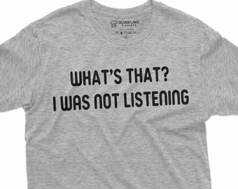 Puede incluir: Una camiseta gris jaspeado con el texto negro "WHAT'S THAT? I WAS NOT LISTENING" centrado en la parte delantera. La camiseta tiene mangas cortas y cuello redondo. La etiqueta de la marca Silver Lake T-shirts es visible en la parte superior.