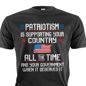 Puede incluir: Camiseta negra con un estampado gr&aacute;fico blanco que dice "PATRIOTISM= IS SUPPORTING YOUR COUNTRY ALL THE TIME AND YOUR GOVERNMENT WHEN IT DESERVES IT". El gr&aacute;fico tambi&eacute;n incluye una bandera estadounidense desgastada.