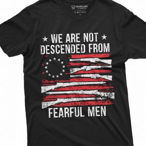 May include: Black t-shirt featuring a distressed American flag design with guns and the text "We are not descended from fearful men."