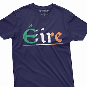 May include: A navy blue t-shirt with the word "Éire" printed in white with green and orange accents. The word is stylized with a distressed look and is centered on the shirt. The Irish flag colors are incorporated into the design.