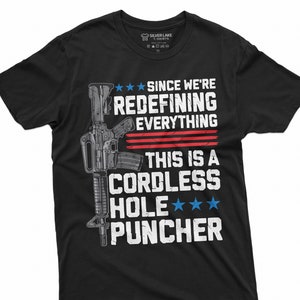 May include: Black t-shirt with a white graphic of a rifle and the text "Since we're redefining everything this is a cordless hole puncher" with three stars.