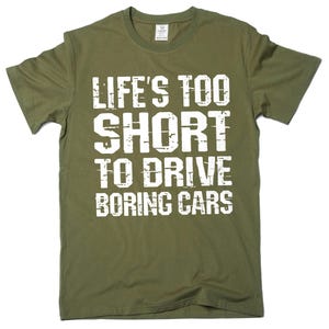 May include: Olive green t-shirt with the white text "LIFE'S TOO SHORT TO DRIVE BORING CARS". The shirt has a crew neck and short sleeves. The text is in a bold, distressed font.