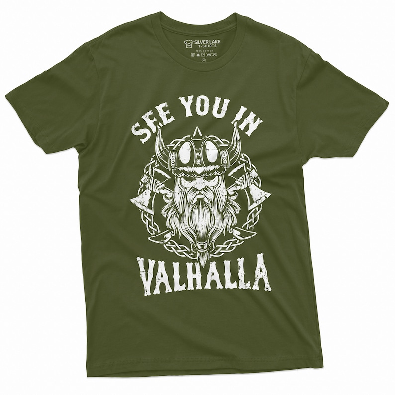 May include: Olive green t-shirt with a white graphic of a Viking warrior wearing a horned helmet, with the text "SEE YOU IN VALHALLA". The design includes axes and a braided border. The shirt is from Silver Lake T-Shirts.