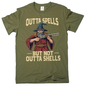 May include: Olive green t-shirt featuring a wizard graphic holding a shotgun. The wizard wears a blue hat and red robe. Text on the shirt reads "OUTTA SPELLS BUT NOT OUTTA SHELLS".