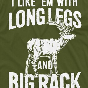 May include: A green t-shirt with white text that reads "I like 'em with long legs and big rack". A white silhouette of a deer with large antlers is in the center of the shirt.