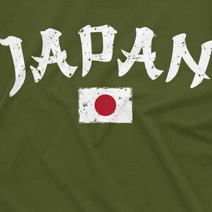 May include: A green t-shirt with the word "JAPAN" in white distressed lettering and a white distressed image of the Japanese flag with a red circle in the center.