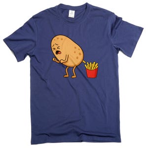 Puede incluir: Camiseta azul marino con un diseño de dibujos animados humorístico. Representa una patata de dibujos animados con una expresión angustiada, produciendo patatas fritas. Las patatas fritas están en un recipiente rojo. El diseño está centrado.