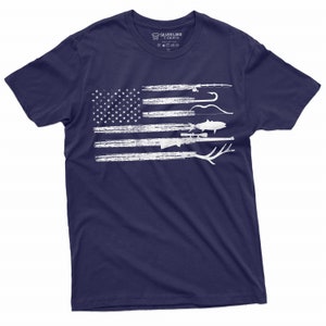 May include: A navy blue t-shirt with a white distressed American flag design. The flag is made up of various hunting and fishing items, including a rifle, a fish, a bow and arrow, and a fishing rod.
