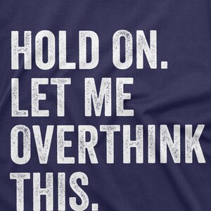 May include: A navy blue t-shirt with white text that reads "HOLD ON. LET ME OVERTHINK THIS."