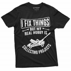May include: Black t-shirt with white text that reads "I fix things but my real hobby is collecting projects". The text is surrounded by wrench symbols. A white silhouette of a car jack is below the text.