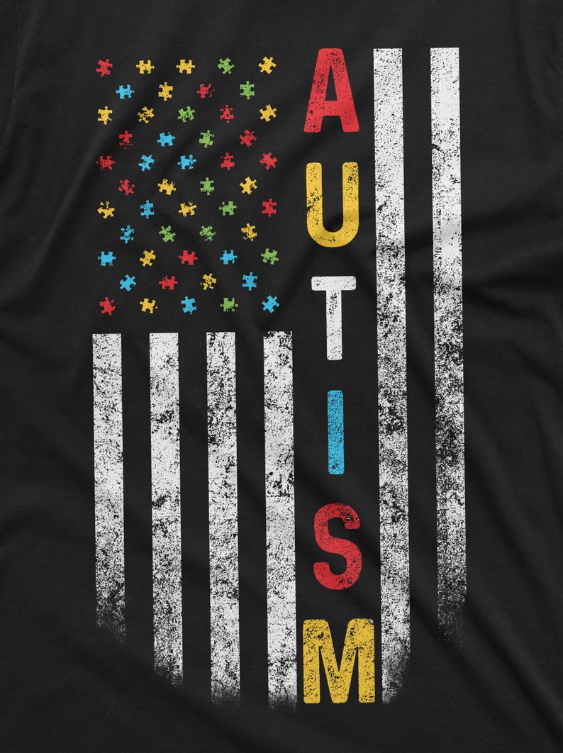 Peut inclure: T-shirt noir avec un motif drapeau am&eacute;ricain vieilli. Les &eacute;toiles sont remplac&eacute;es par des pi&egrave;ces de puzzle color&eacute;es et le mot "AUTISM" est imprim&eacute; verticalement en lettres color&eacute;es et en gras.