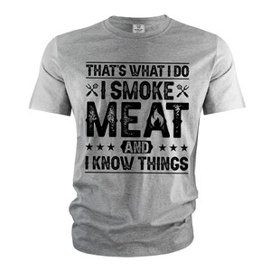 May include: Gray t-shirt with a black graphic that says "That's what I do I smoke meat and I know things". The graphic includes a fork and knife and a flame.