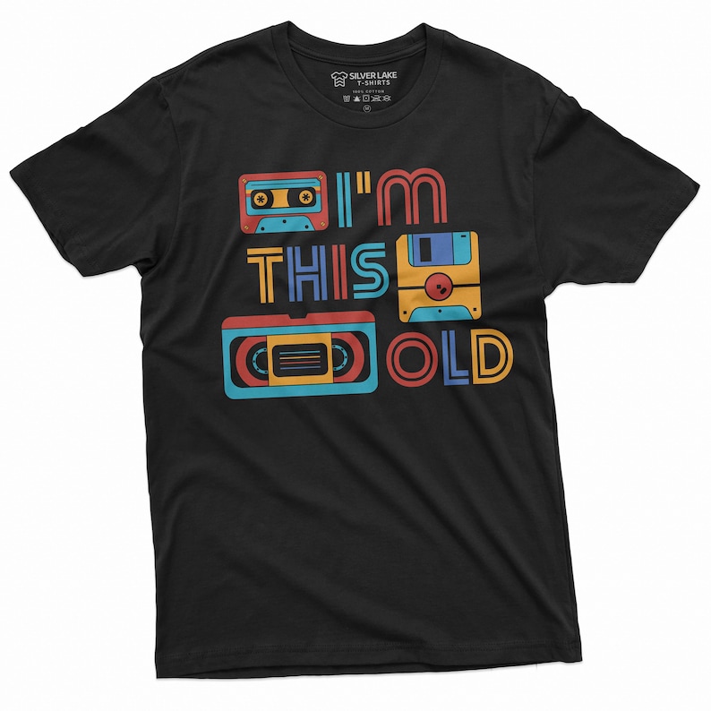 May include: Black t-shirt with a retro design featuring a cassette tape, floppy disk, and VHS tape. The text "I'm This Old" is printed on the shirt.