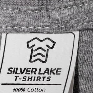 May include: A white tag with black text and a graphic of a t-shirt. The tag reads "Silver Lake T-Shirts 100% Cotton".